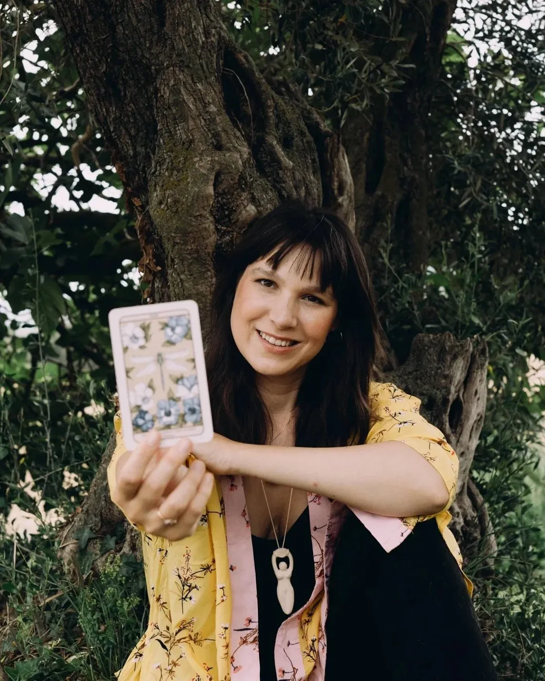 La Clara asseguda sota un arbre, somrient, amb una carta de tarot a la mà